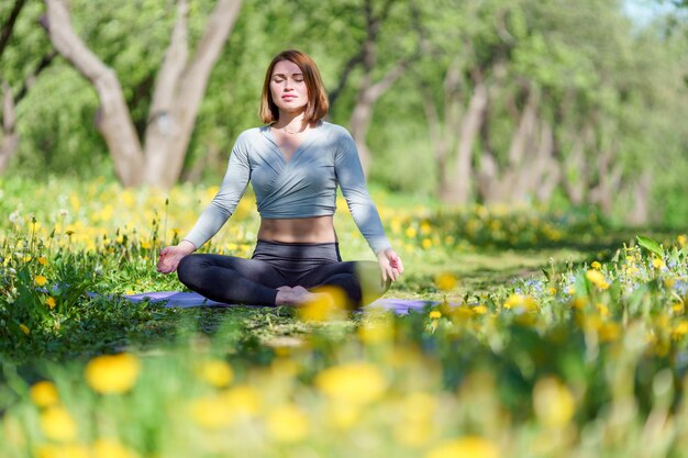 Bild einer Frau beim Yoga sitzend im Lotussitz auf blauem Teppich im Wald am Sommertag