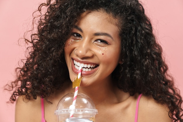 Bild einer glücklichen afroamerikanischen Frau mit Handschuhen, die lächelt und Soda trinkt