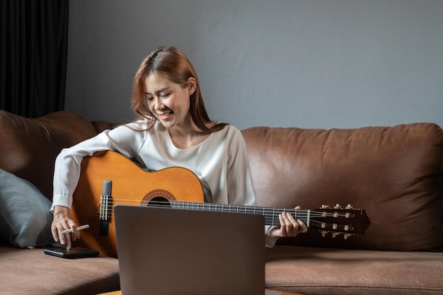Bild einer glücklichen, schönen Frau, die Gitarre spielt und ein Lied komponiert