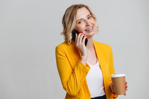 Bild einer glücklichen zufriedenen Geschäftsfrau lokalisiert über weißem Wandhintergrund, der durch Handy spricht.