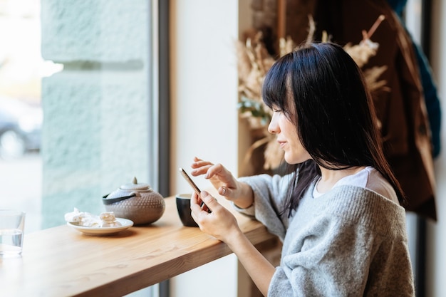 Bild einer jungen Frau, die im Café SMS am Telefon liest