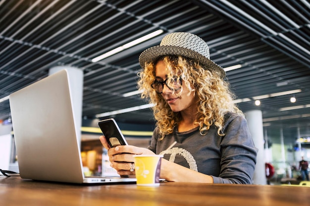 Bild einer jungen, trendigen Reisenden, die mit Handy und Laptop in einer Café-Bar arbeitet, die eine kostenlose drahtlose Verbindung hat