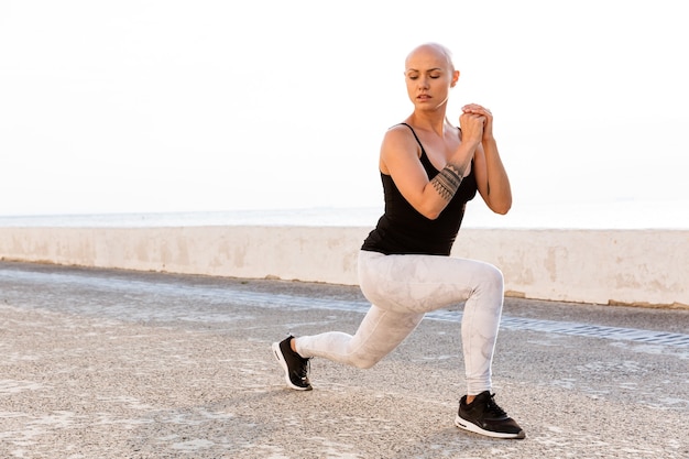 Bild einer konzentrierten glatzköpfigen Frau in Sportkleidung, die beim Training am sonnigen Morgen im Freien Übungen macht