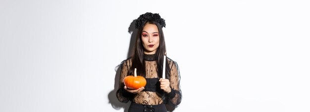 Foto bild einer schönen asiatischen frau in hexenkostüm, die eine angezündete kerze und einen kürbis hält und halloween feiert