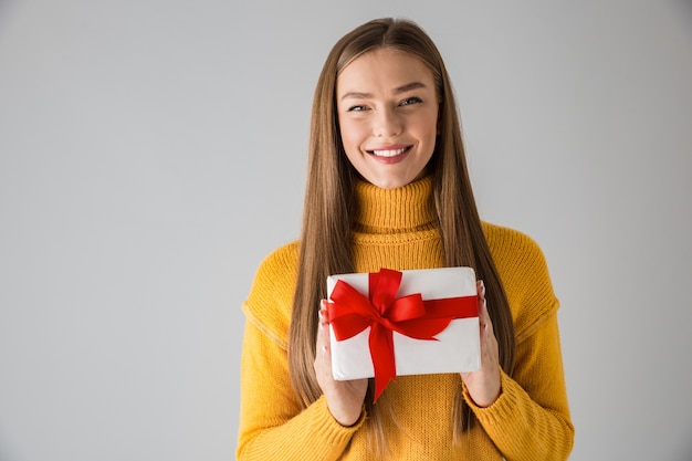 Bild einer schönen glücklichen jungen Frau lokalisiert über graue Wand, die Geschenkgeschenkbox hält.