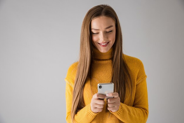 Bild einer schönen glücklichen jungen Frau lokalisiert über graue Wand unter Verwendung des Mobiltelefons.