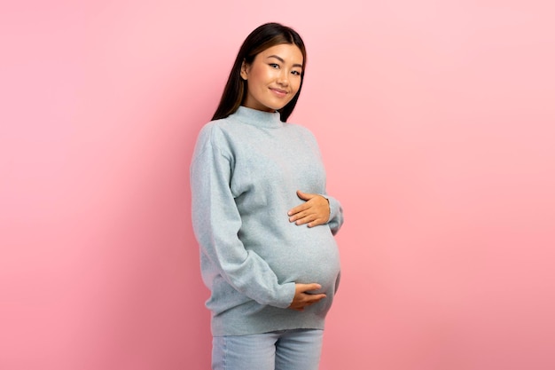 Bild einer schönen jungen schwangeren asiatischen Frau, die isoliert über Rosa posiert