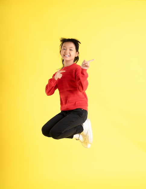 Foto bild eines asiatischen mädchens, das einen pullover trägt und auf einem gelben hintergrund posiert