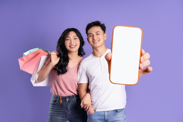 Bild eines asiatischen Paares, das Einkaufstaschen auf violettem Hintergrund hält