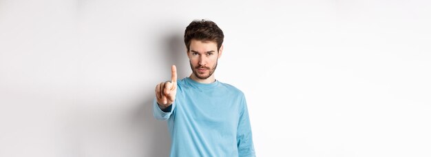 Foto bild eines ernsthaften jungen mannes mit bart, der finger in ablehnung schüttelt, um etwas zu verbieten oder zu verbieten