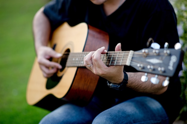 Bild eines Gitarristen, eines jungen Mannes, der eine Gitarre beim Sitzen in einem natürlichen Garten, Musikkonzept spielt