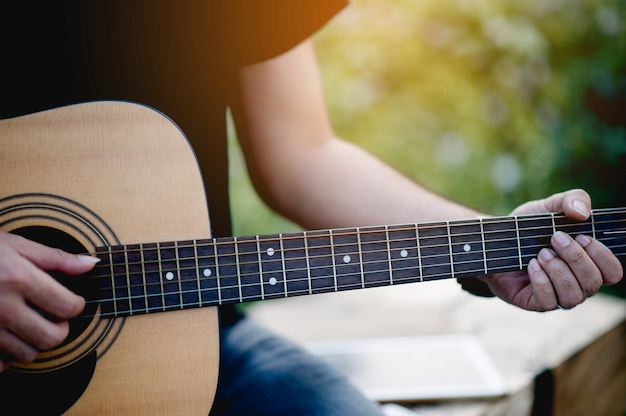 Bild eines Gitarristen, eines jungen Mannes, der eine Gitarre beim Sitzen in einem natürlichen Garten, Musikkonzept spielt