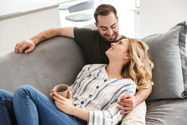 Bild eines glücklichen aufgeregten jungen Liebespaares, das zu Hause auf dem Sofa sitzt und umarmt.