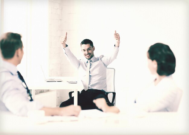 Bild eines glücklichen Geschäftsmannes, der im Büro Daumen nach oben zeigt