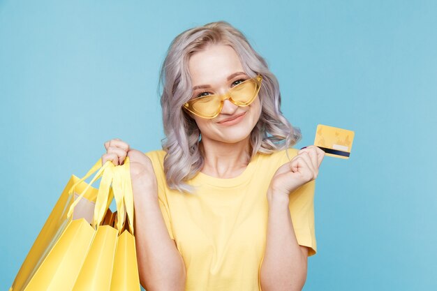 Bild eines glücklichen Mädchens mit Kreditkarte und großen Einkaufstüten über dem blauen Studio isoliert.