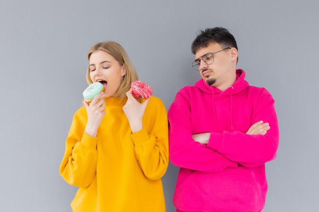 Bild eines glücklichen Paares, Mann und Frau, die lächeln, während sie gemeinsam süße Donuts essen