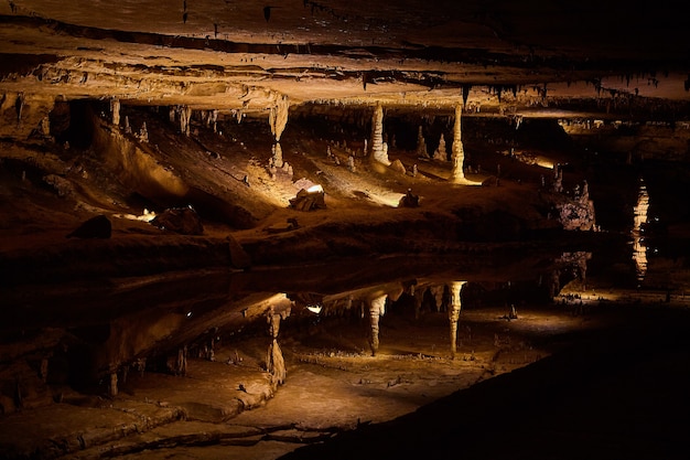 Bild eines großen reflektierenden Teichs, der wie ein Spiegel in einer Höhle mit Stalagmiten und Stalaktiten aussieht