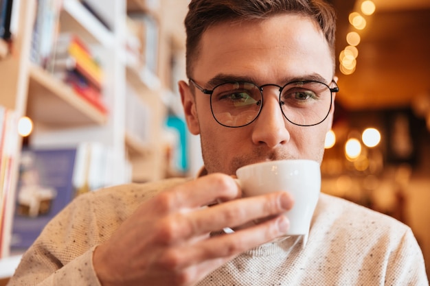 Bild eines hübschen jungen Mannes, der beim Kaffeetrinken im Café sitzt und beiseite schaut.