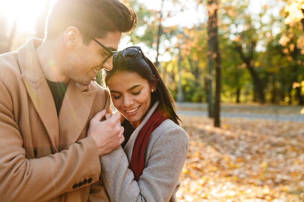 Bild eines jungen glücklichen Paares, das sich beim Gehen im Herbstpark lächelt und umarmt