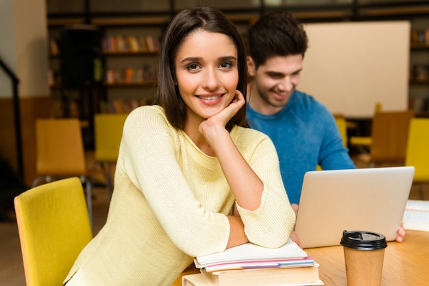 Bild eines jungen Studentenfreundepaares in der Bibliothek, die Hausaufgaben macht, die lesen und Laptop-Computer verwenden.