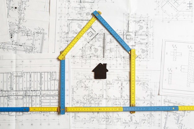 Bild eines kleinen schwarzen Spielzeughauses und eines zusammenklappbaren gelben und blauen Lineals, das auf dem Architekturplan steht