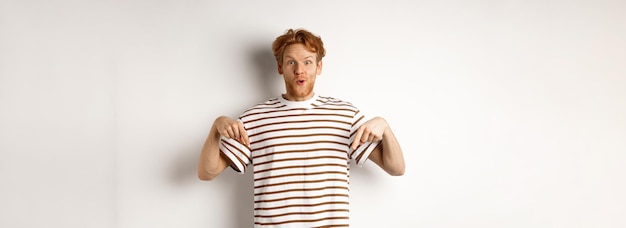 Bild eines lustigen rothaarigen männlichen Studenten, der mit den Fingern nach unten zeigt und ein Werbeangebot mit einem aufgeregten Lächeln zeigt