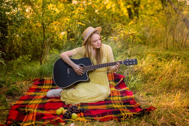 Bild eines Mädchens mit Strohhut, das im Park Gitarre spielt