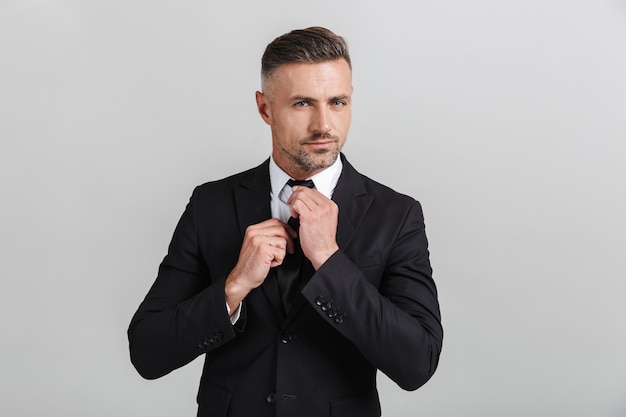 Bild eines männlichen erwachsenen Geschäftsmannes im Anzug, der seine Krawatte isoliert glättet