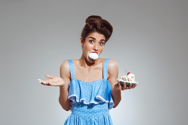 Bild eines schönen Pinup-Mädchens, das Kuchen im Studio isst