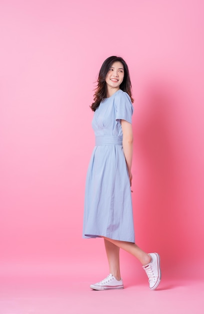 Bild in voller Länge der jungen asiatischen Frau, die blaues Kleid auf rosa Hintergrund trägt