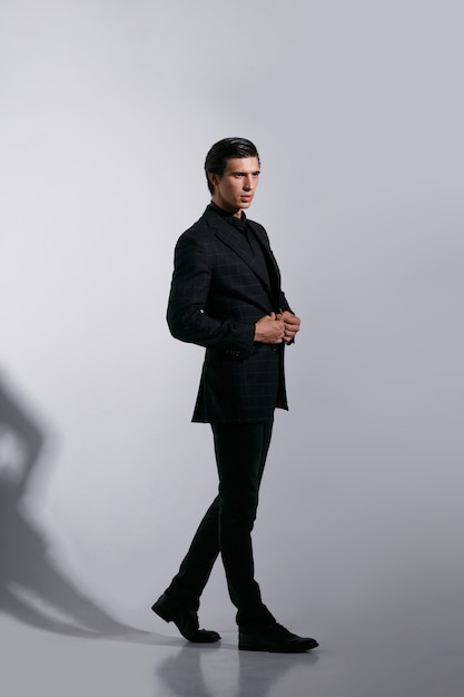 Bild in voller Länge des hübschen männlichen Modells im schwarzen stilvollen Anzug, lokalisiert auf weißem Hintergrund.