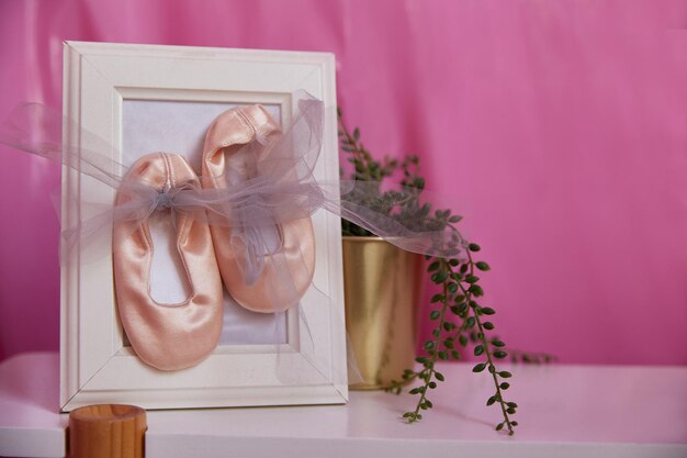 Bild mit rosa Babyschuhen und einer Blume auf einem Regal im Zimmer. Innenarchitektur.