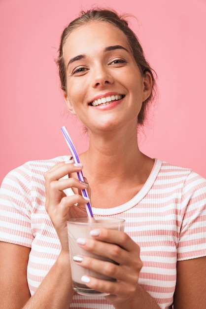 Bild Nahaufnahme einer fröhlichen, wunderschönen Frau, die lächelt und Schokoladenmilch mit Strohhalm über rosa Wand trinkt?