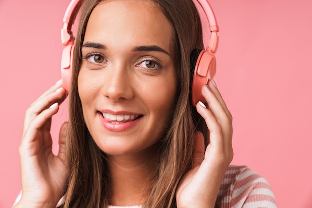 Bild Nahaufnahme eines hübschen schönen Mädchens in gestreifter Kleidung, das lächelt und Musik mit Kopfhörern hört, die über rosa Wand isoliert sind?