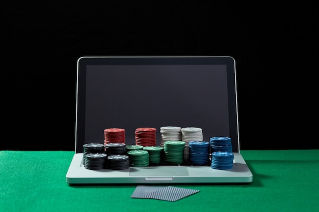 Bild von Casino-Chips und Karten auf einem Tastaturnotizbuch am grünen Tisch. Konzept für Online-Glücksspiele, Poker, virtuelles Casino.