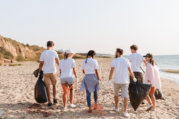 Bild von der Rückseite multinationaler junger Freiwilliger, die den Strand mit Müllsäcken an der Küste von Plastik reinigen