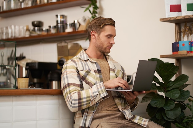 Bild von einem jungen stilvollen Mann mit Laptop, der mit seinem Computer im Café sitzt und etwas trinkt