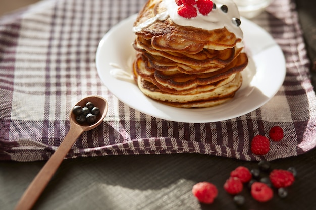 Bild von Käsepfannkuchen mit saurer Sahne und frischen Beeren, Brombeermarmelade in Holzlöffel, Schlagsahne auf Muffins oben