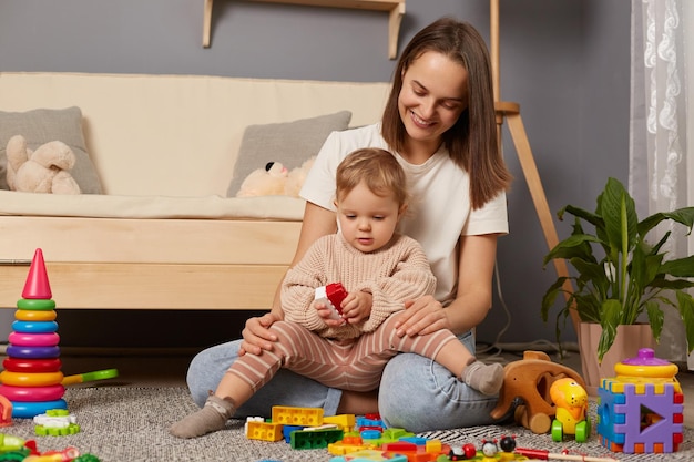 Bild von lächelnder Mutter und Kind, die im Kindergarten auf dem Boden spielen, mit dem Bau eines Turms aus farbigen Blöcken Bildungsaktivitäten von Kindern mit Eltern zu Hause