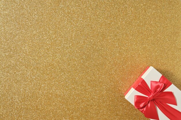 Bild von oben des Geschenks mit roter Schleife auf glänzendem goldenem Hintergrund