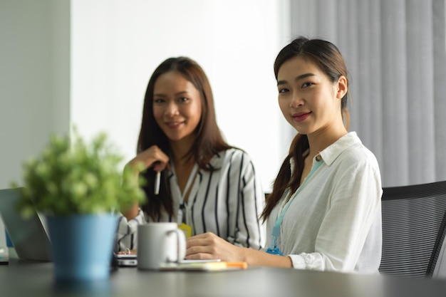 Bild von zuversichtlich asiatischen Geschäftsfrauen lächeln in die Kamera, während sie am Schreibtisch im Büro sitzen.