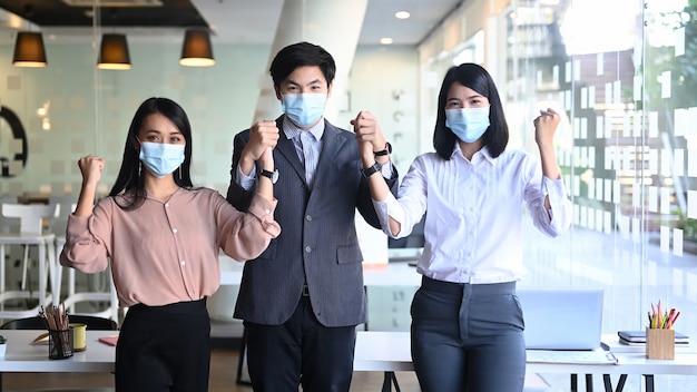 Bild von zuversichtlichen Geschäftsleuten oder Büroangestellten, die medizinische Maske tragen, während sie im modernen Büro stehen.