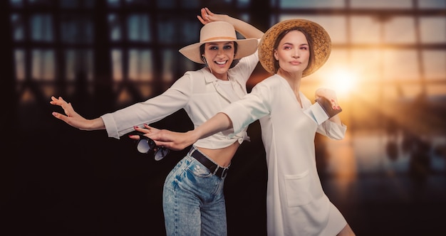 Bild von zwei schönen Frauen mit Hüten am Flughafen. Lustige Gesichter. Reisekonzept. Gemischte Medien