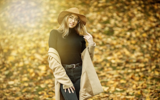 Bildaufnahme einer jungen attraktiven Frau in Mantel und Filzhut auf dem Hintergrund abgefallener Blätter im Herbstpark