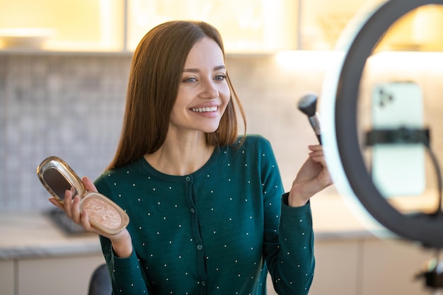 Bilden. Frau hält Gesichtsbürste und macht Make-up