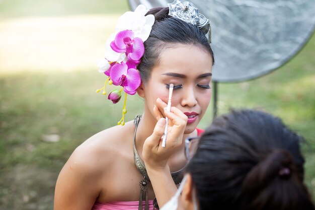 Bilden Sie den Künstler, der Eyeliner zur thailändischen Frau bildet, die thailändische traditionelle Kleidung trägt