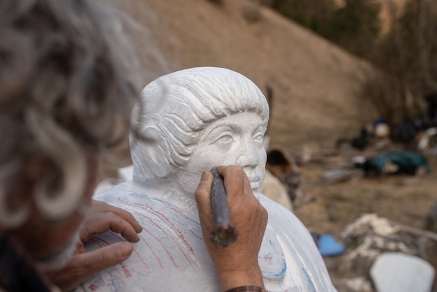 Bildhauer arbeitet an seiner Statue mit einem Meißel, um an Details zu arbeiten.