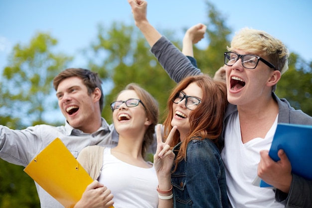 bildung, freundschaft, erfolg und jugendliches konzept - gruppe glücklicher studenten, die triumphgesten auf dem campus oder im park zeigen