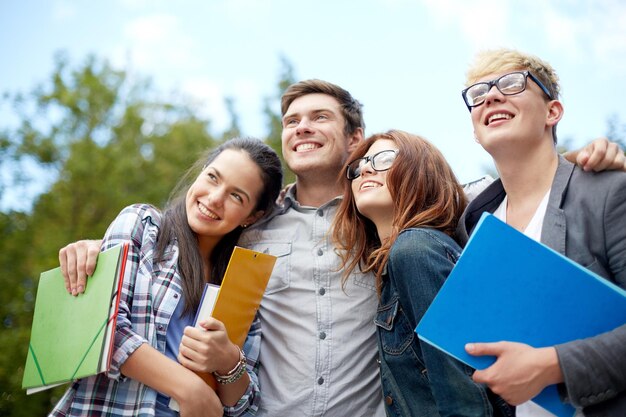 bildung, freundschaft, zukunft und jugendliches konzept - gruppe glücklicher studenten mit ordnern, die auf den campus oder park schauen