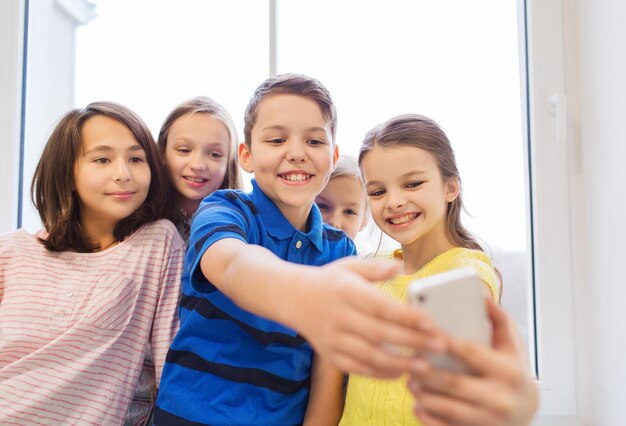 bildung, grundschule, getränke, kinder- und menschenkonzept - gruppe von schulkindern, die selfie mit smartphone im korridor machen